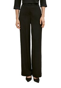 Czarne spodnie z szerokimi nogawkami, wykonane z gładkiego materiału, o wysokim stanie i fałdach z przodu. W połączeniu z czarnymi, szpiczastymi obcasami, co nadaje elegancki wygląd.