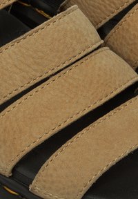 Sandali in pelle color tan con larghe cinghie testurizzate e cuciture visibili. La soletta è nera con una leggera contorno.