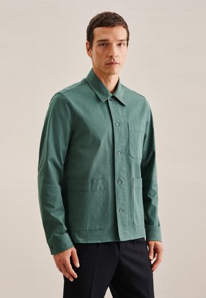 Groene katoenen jas met een knoopsluiting aan de voorkant, kraag, twee voorzakken en lange mouwen. Heeft een gladde textuur en een getailleerde pasvorm.