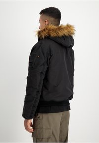 Zwarte capuchonjack met een nepleren rand, ribbelcuffs en zijzakken. De stof lijkt soepel met minimale zichtbare branding.