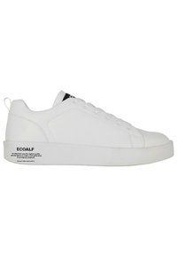 Hvide sneakers med en glat læderoverdel, lavt design, fem snørehuller og en tyk hvid sål; har et sort logo mærke på tungen.