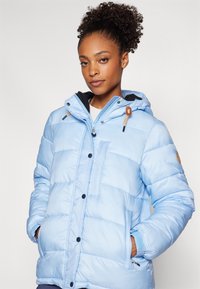 Giacca puffer azzurro chiaro con cappuccio zipato, tasche frontali e chiusure con bottoni. Presenta un design trapuntato e un rivestimento nero a contrasto.