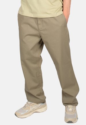 Khakifarbene Baumwollhosen mit entspannter Passform, versehen mit Seitentaschen und einer glatten Textur, kombiniert mit hellbeigen Sportschuhen.