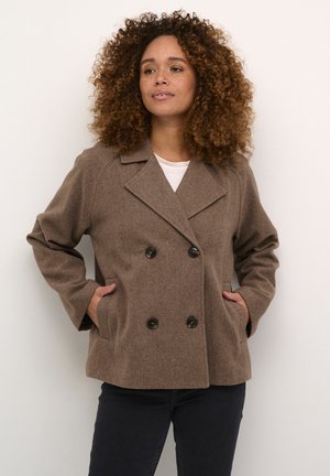 Brown double-breasted wool jacket with large black buttons, oversized fit, lapel collar, and side pockets, worn over a white shirt.