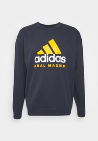 Sudadera de color navy con cuello redondo, mangas largas y un logo brillante de Adidas en amarillo y blanco con el texto "REAL MADRID" debajo.