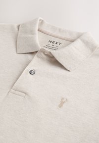 Beige pikétröja i medelstor passform med krage, en knapp och subtil hjortlogotyp broderad på bröstet, märkt "Next" och tillverkad i Bangladesh.