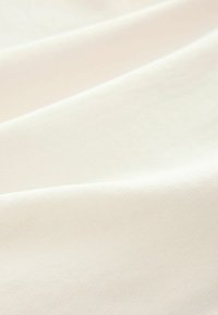 Cotton fabric in off-white, showing a smooth texture with subtle ribbing and gentle folds, emphasizing softness and lightweight characteristics.