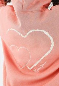 Sudadera coral con un gran diseño de contorno de corazón blanco en la espalda y detalles texturizados. Cuenta con una capucha con cordón y tela suave.
