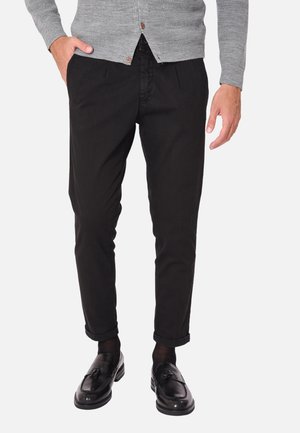 Chinos neri tapered con una texture liscia. Abbinati a mocassini neri lucidi e un cardigan grigio. Presentano polsini arrotolati e tasche laterali.