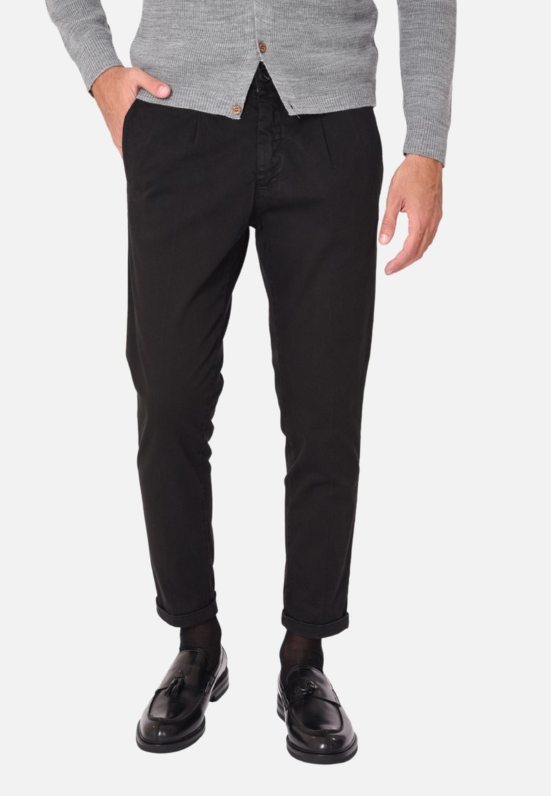 Chinos neri tapered con una texture liscia. Abbinati a mocassini neri lucidi e un cardigan grigio. Presentano polsini arrotolati e tasche laterali.