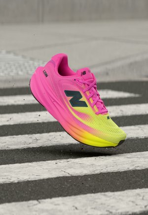 Chaussure de running New Balance rose vif et jaune en l’air au-dessus d’un passage piéton sur une rue en asphalte.