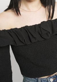 Top nero senza spalline con scollatura arricciata, caratterizzato da una texture arricciata e maniche lunghe, abbinato a pantaloni shorts in denim.