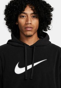 Schwarze Fleece-Hoodie mit großem weißem Nike-Swoosh-Logo, verstellbarem Kordelzug und klassischem Kängurutaschen-Design.