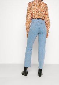 Jasnoniebieskie jeansy z wysokim stanem o prostym kroju, zestawione z wielokolorową kwiecistą bluzką i czarnymi botkami na obcasie.