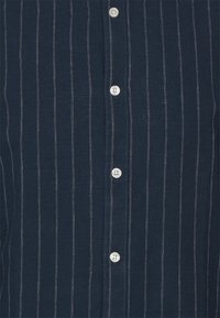Camisa de botones color navy hecha de una tela suave, con rayas blancas verticales, seis botones en la parte delantera y costuras en contraste.