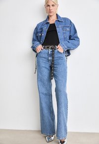 Μπλε τζιν μπουφάν με άνετη εφαρμογή πάνω από μια μαύρη μπλούζα. Πλατύς μπλε τζιν που είναι κλεισμένος με μια μαύρη ζώνη με ασημένιες λεπτομέρειες. Ασημένια παπούτσια.