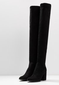 Bottes noires mi-cuisses en daim, avec un bout arrondi, un talon carré et un design sans coutures ni éléments visibles.