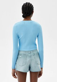 Light blue ribbed long-sleeve top with a fitted design, paired with distressed light denim shorts, viewed from the back.