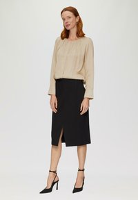 Beige blouse met lange mouwen en plooien, gecombineerd met een zwarte rok tot de knie met een voorkoonsluiting. Draagt zwarte stilettohakken.