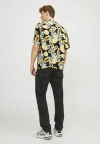 Schwarzes Kurzarmhemd mit lebendigem gelben Obst- und grünem Blattdruck; kombiniert mit dunklen Hosen und grauen Sneakers. Lässiger Schnitt und entspanntes Design.