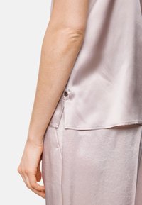 Light pink satin top with a smooth texture, featuring a side button closure and a relaxed fit. The hem falls slightly below the waist.