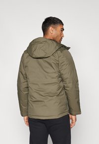 Olivgrüne isolierte Jacke mit Kapuze, mit einer glatten Textur, elastischen Bündchen und genähten Details entlang der Nähte.
