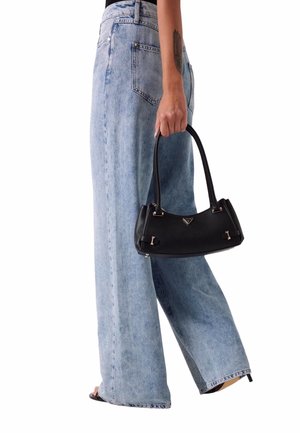 Borsa nera con design strutturato, texture liscia e dettagli dorati, tenuta con una mano; indossata con jeans a gamba larga di un azzurro chiaro.