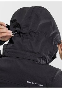 Schwarze Outdoor-Jacke mit verstellbarem Kapuzenzug, glatter Textur, minimaler Markenkennzeichnung und schlankem Design. Verstellbares Merkmal dargestellt.