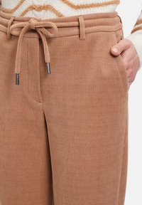 Tan corduroy broek met een ribbeltextuur, voorzien van een tailleband met trekkoord, zijzakken en metalen accenten op de uiteinden van het trekkoord.