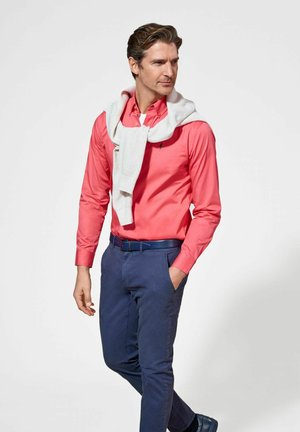 Różowa koszula na guziki, granatowe spodnie i jasnoszary sweter przewiązany na szyi. Elegancki fason z wypolerowanym wyglądem.