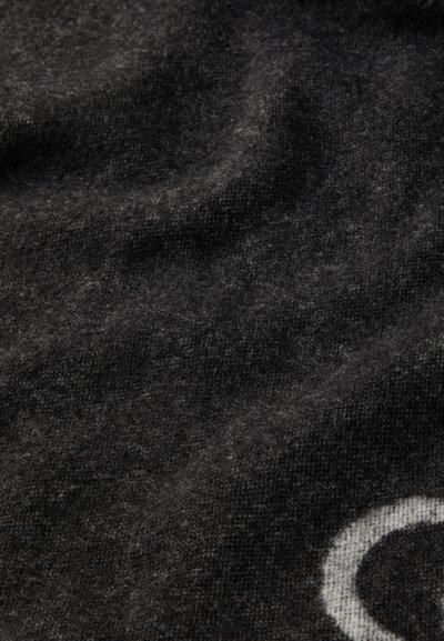 Grå stickad tyg med en mjuk, texturerad yta, med en vit cirkulär design i ett hörn och en något luddig framtoning.
