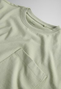 Lichtgroen T-shirt met ronde hals en een enkele borstzak, plat weergegeven op een witte ondergrond.
