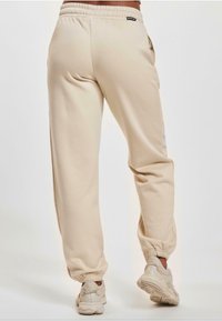 Beige Jogginghosen mit elastischem Bund und Bündchen, ausgestattet mit seitlichen Taschen und einer weichen Textur. Kombiniert mit hellen Sportschuhen.