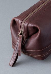 Brown leather pouch with a gold zipper, textured surface, and contrasting stitching. Features a leather pull tab on the zipper.