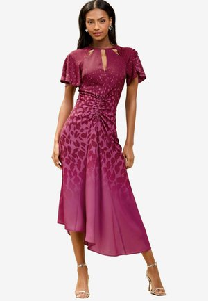 Robe mauve avec un décolleté en clé, des manches flottantes et des coutures latérales froncées. Un design dégradé avec des motifs de feuilles au bas.