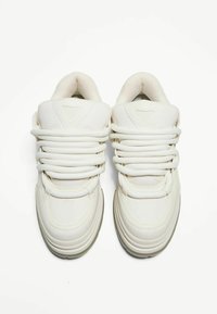 Chaussures de sport blanches avec une tige synthétique lisse, de larges lacets, un col rembourré et une semelle arrondie arborant une légère teinte grise.