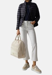 Veste matelassée marine, jean blanc, baskets beiges et un sac à main beige clair avec des accents dorés et deux poignées, présentant une texture lisse.