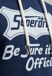 Felpa con cappuccio blu navy in tessuto testurizzato, con testo stampato bianco "Superdry" e "Assicurati che sia Ufficiale." Coulisse con punte metalliche.