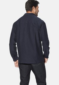 Herrenhemd in Dunkelblau, mit langen Ärmeln, Knopfmanschetten, Kragen, glatter Textur, Details am Rückenteil, taillierte Passform, kombiniert mit dunklen Jeans.