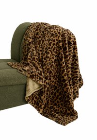 Manta con estampado de leopardo y textura suave y aterciopelada, con tonos marrones y negros en un lado, beige en el reverso. Colgada sobre un sofá verde.