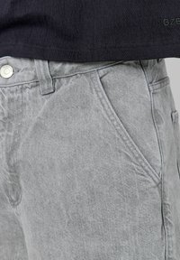 Shorts en denim gris avec une coupe décontractée, dotés de poches avant et d'un bouton en métal argenté. Le tissu a un aspect doux et texturé.