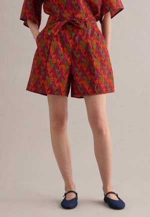 Persona che indossa pantaloncini a vita alta e top coordinato con motivi di foglie rosse, arancioni e verdi, abbinati a scarpe Mary Jane blu navy.