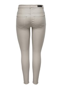 Beige skinny jeans gemaakt van rekbaar materiaal, met twee achterzakken en een gladde textuur. Zichtbare stiksels langs de naden.