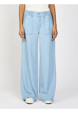 Light blue wide-leg denim pants with front patch pockets worn with white sneakers and a white top, shown from waist to feet.