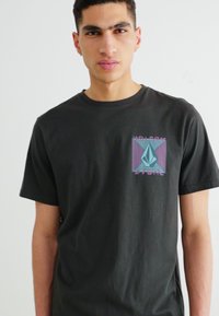 Camiseta de algodón negra que presenta un gráfico geométrico colorido en el pecho, con diseño de cuello redondo y mangas cortas.