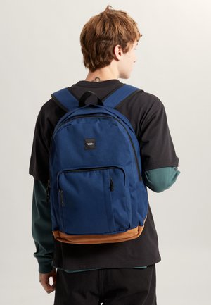 Zaino in tessuto blu con due tasche frontali con zip, fondo con accentuazione color beige, spallacci regolabili e una piccola etichetta con logo sulla parte anteriore.