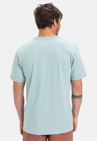 Světle modré tričko s krátkým rukávem z měkké látky. Má klasický kulatý výstřih a rovný zadní lem. Minimalistický design.