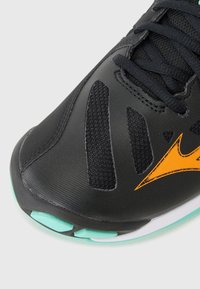 Black athletic shoe featuring a textured upper, breathable mesh sections, and a striking orange logo. The sole has a light blue accent.