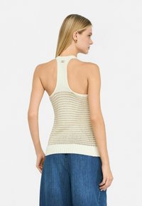 Top in maglia beige chiaro con strisce traforate e orlo a costine; presenta un design a schiena scoperta e un piccolo dettaglio sul colletto.