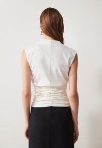 Top blanco sin mangas con un detalle de espalda fruncido, que presenta una textura suave y un diseño ajustado, acompañado de una falda negra de corte entallado.